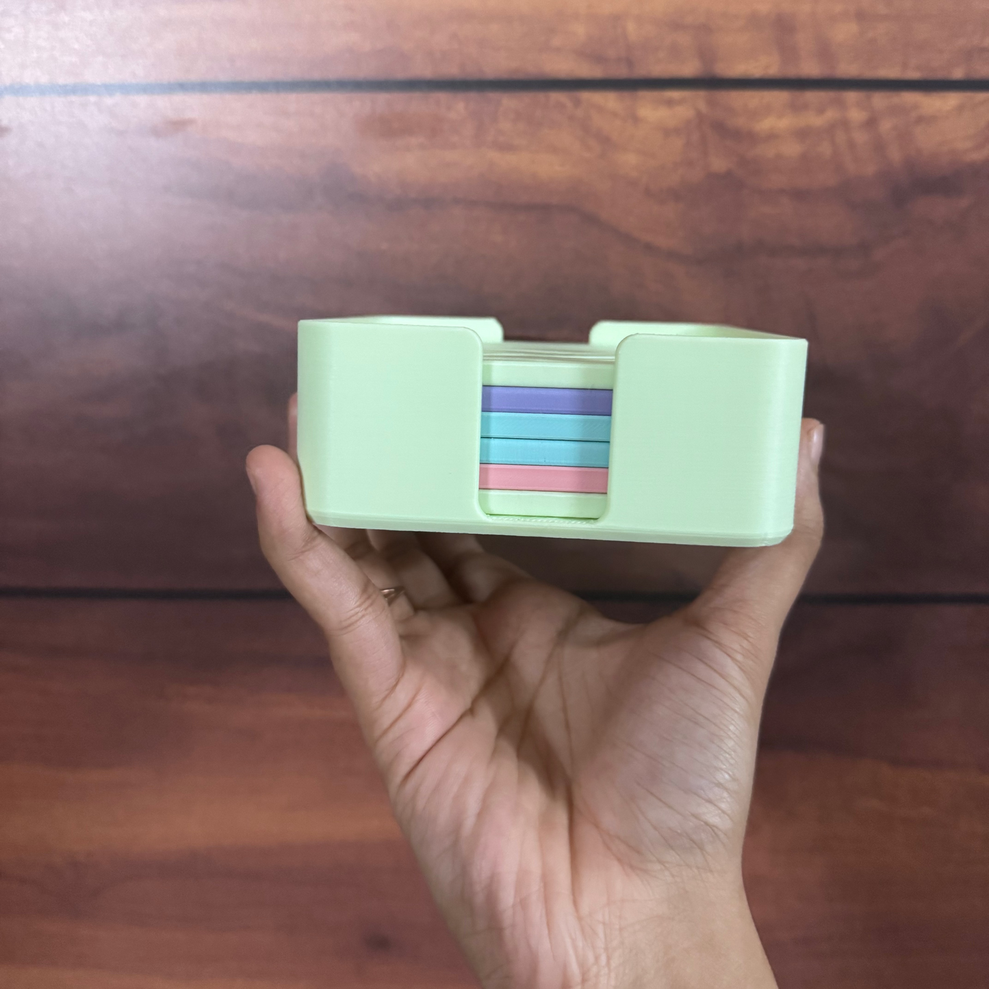 A hand holding a mint green plastic card holder or organizer with a stack of colorful cards inside, set against a dark wood background.