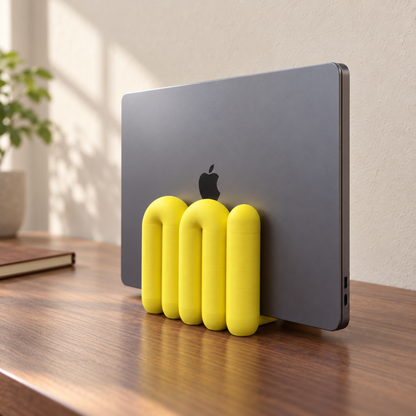 Yellow The Loop Stand holding a closed grey laptop on a walnut desk, angled view
